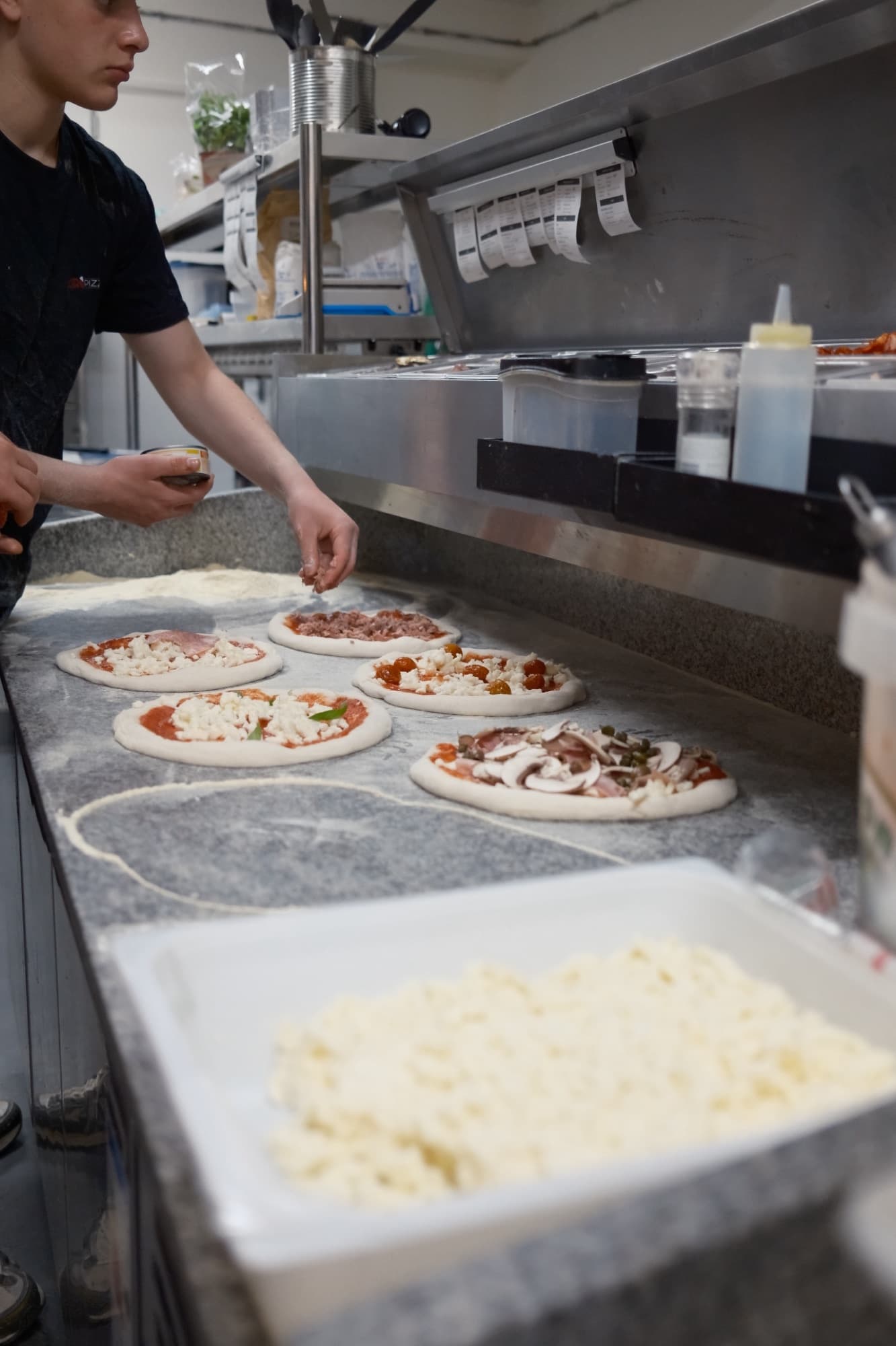 Pizza bases being topped on the marble prep counter