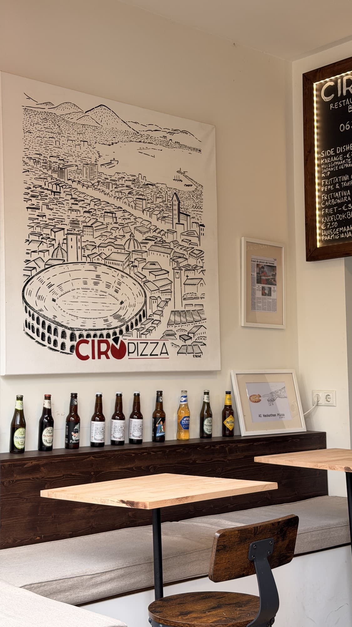 Inside Ciropizza: wooden tables and benches under the big Ciropizza wall canvas